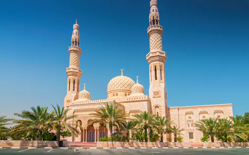 Jumeirah Mosque in Dubai with palm trees and clear blue sky.