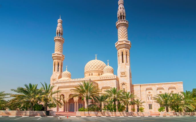 Jumeirah Mosque in Dubai with palm trees and clear blue sky.
