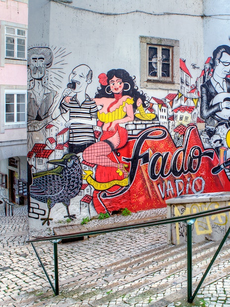 Fado-themed street art on a Lisbon alley wall, featuring musicians and vibrant cityscape.
