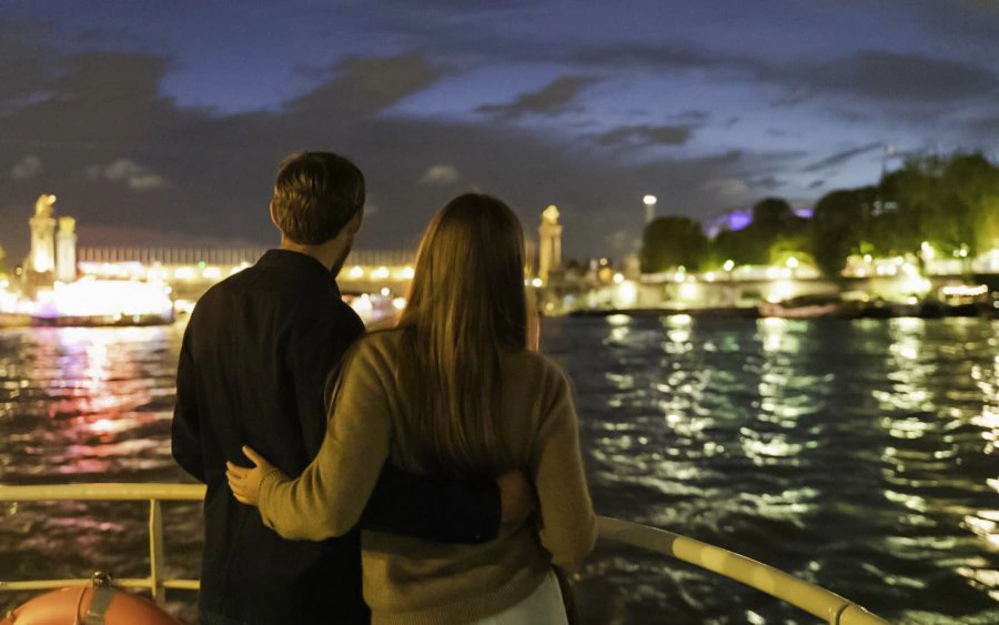 Couple enjoying Paris skyline from Seine River cruise at night, Paris, France.