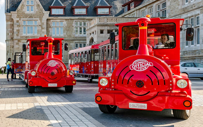 Red sightseeing train parked in front of historic building on panoramic train tour.