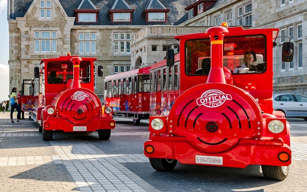 Red sightseeing train parked in front of historic building on panoramic train tour.