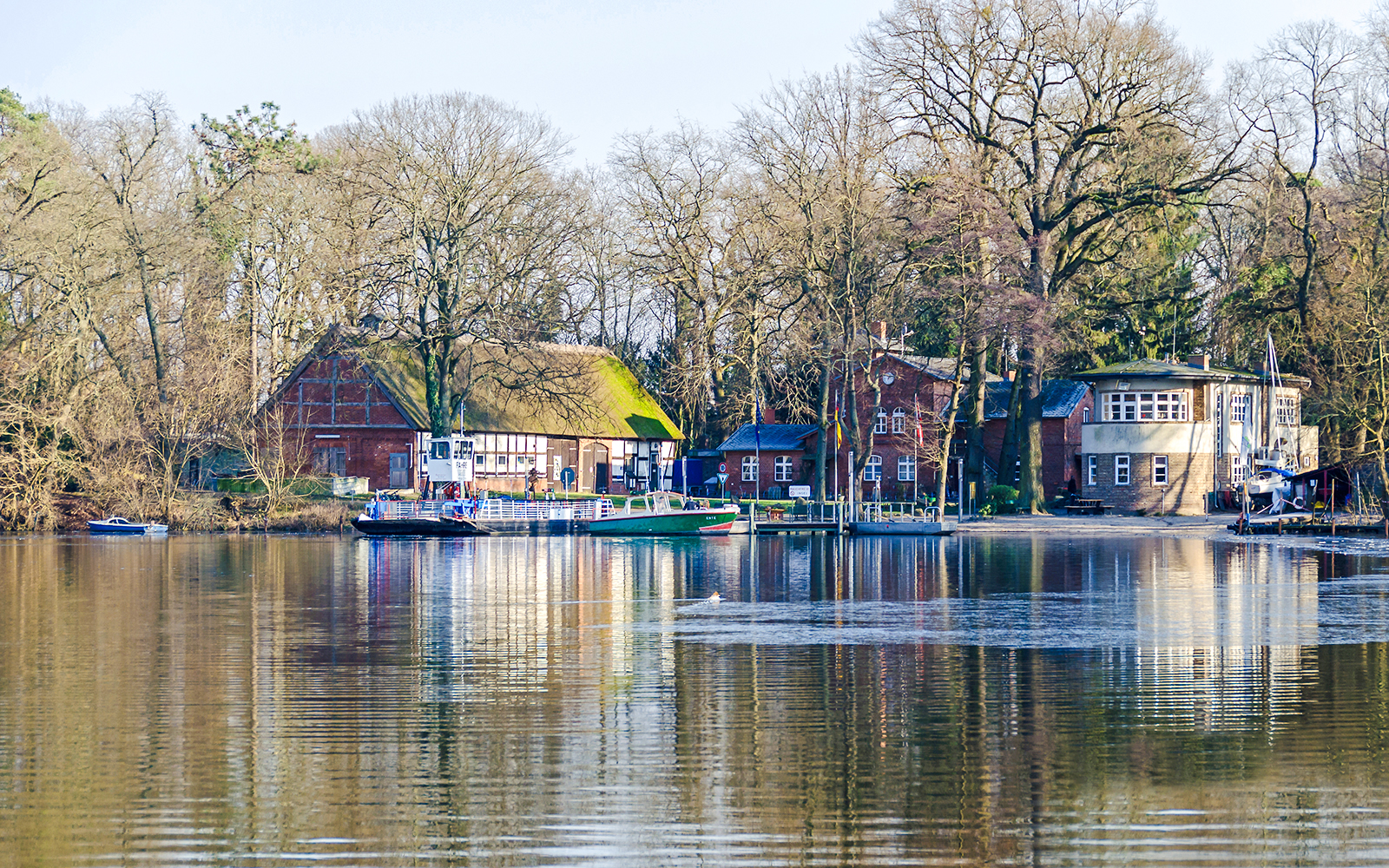 Ferry docked at Island Scharfenberg in Berlin with historic buildings and trees in the background.