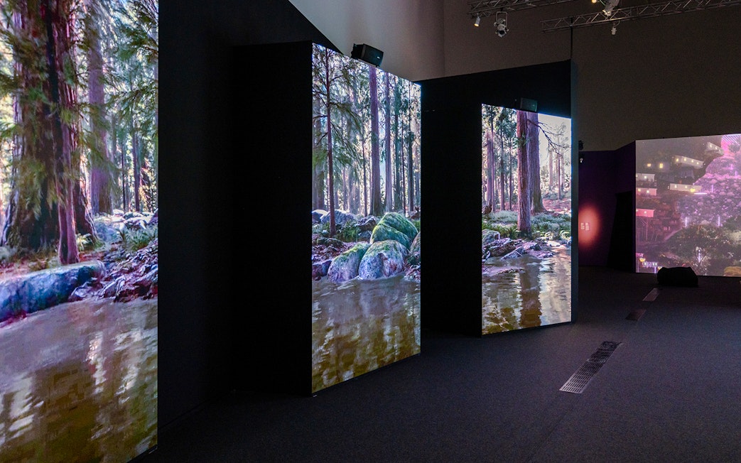 Screens display forest stream and rocky terrain in a dark exhibition hall.