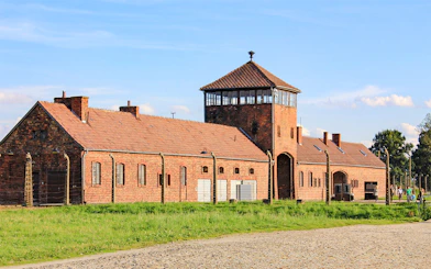 Auschwitz Birkenau II entrance gate with brick buildings and watchtower.