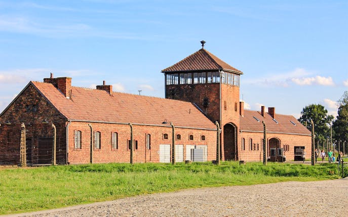Auschwitz Birkenau II entrance gate with brick buildings and watchtower.