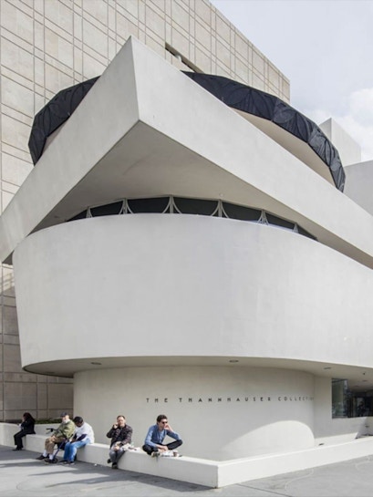 Guggenheim Museum exterior with visitors sitting near the Thannhauser Collection entrance.