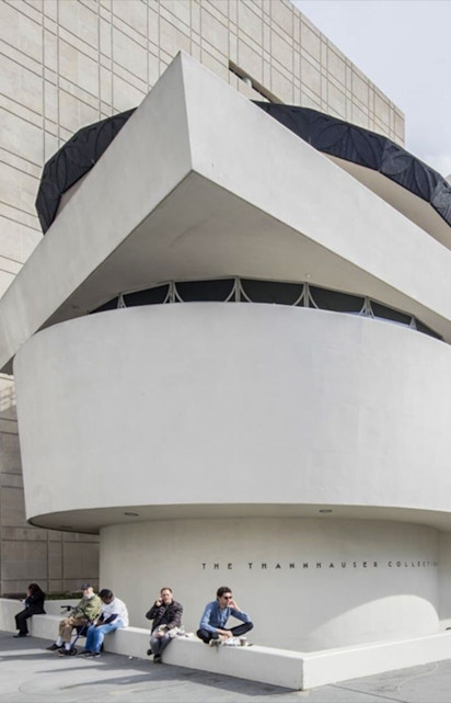 Guggenheim Museum exterior with visitors sitting near the Thannhauser Collection entrance.