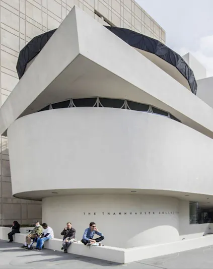 Guggenheim Museum exterior with visitors sitting near the Thannhauser Collection entrance.