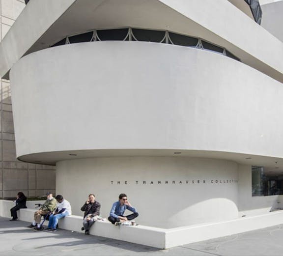 Guggenheim Museum exterior with visitors sitting near the Thannhauser Collection entrance.