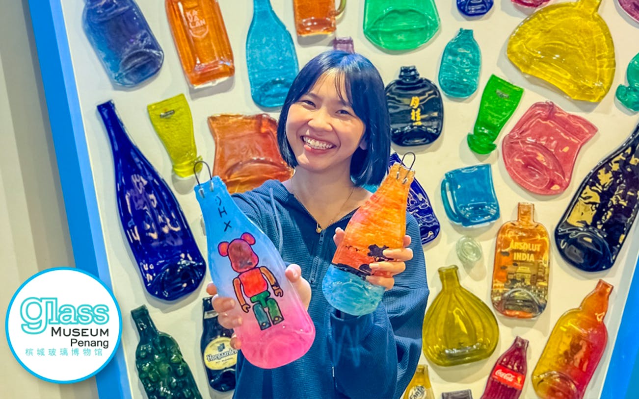 Smiling visitor holding colorful glass art at Glass Museum Penang.