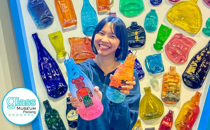 Smiling visitor holding colorful glass art at Glass Museum Penang.