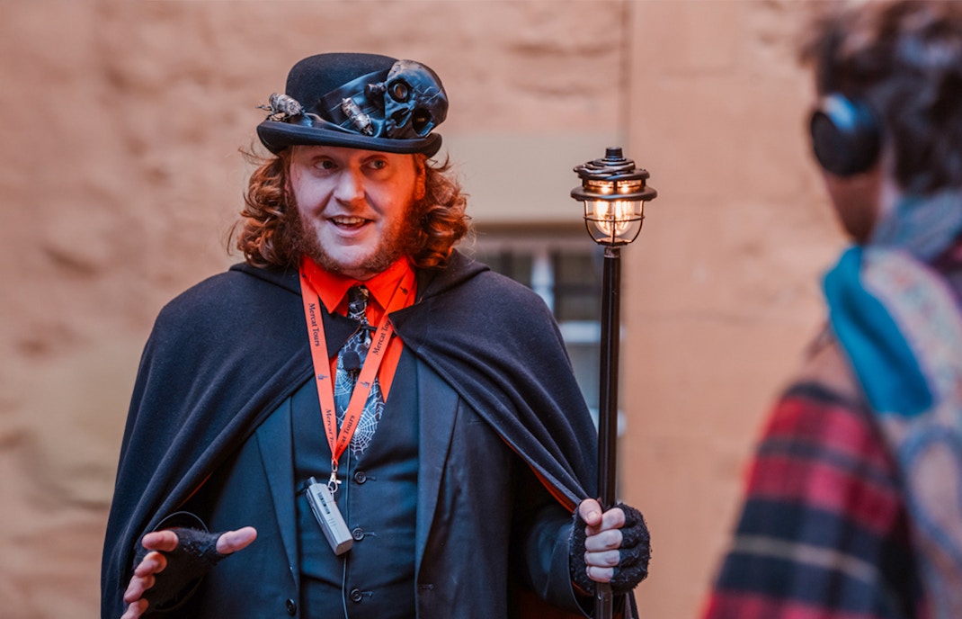 Tour guide in costume leading Edinburgh's Royal Mile ghost tour.