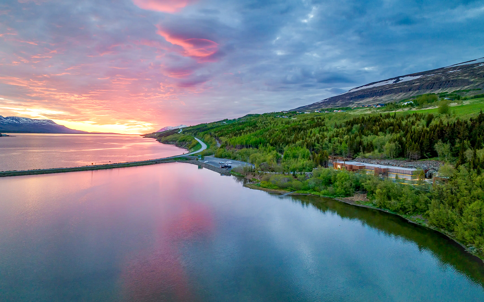 Forest lagoon with lush green trees and pink skies near Akureyri waters.