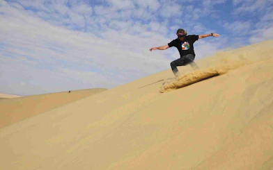 Sandboarding down a desert dune during a Sandboarding & Quad Biking Tour.
