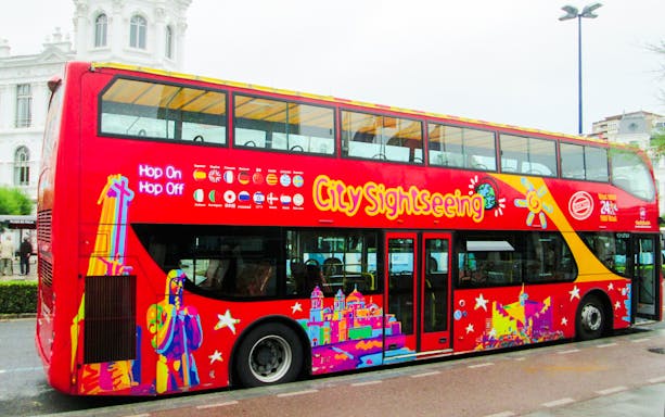 Red double-decker bus for City Sightseeing tour in Santander, parked near a historic building.