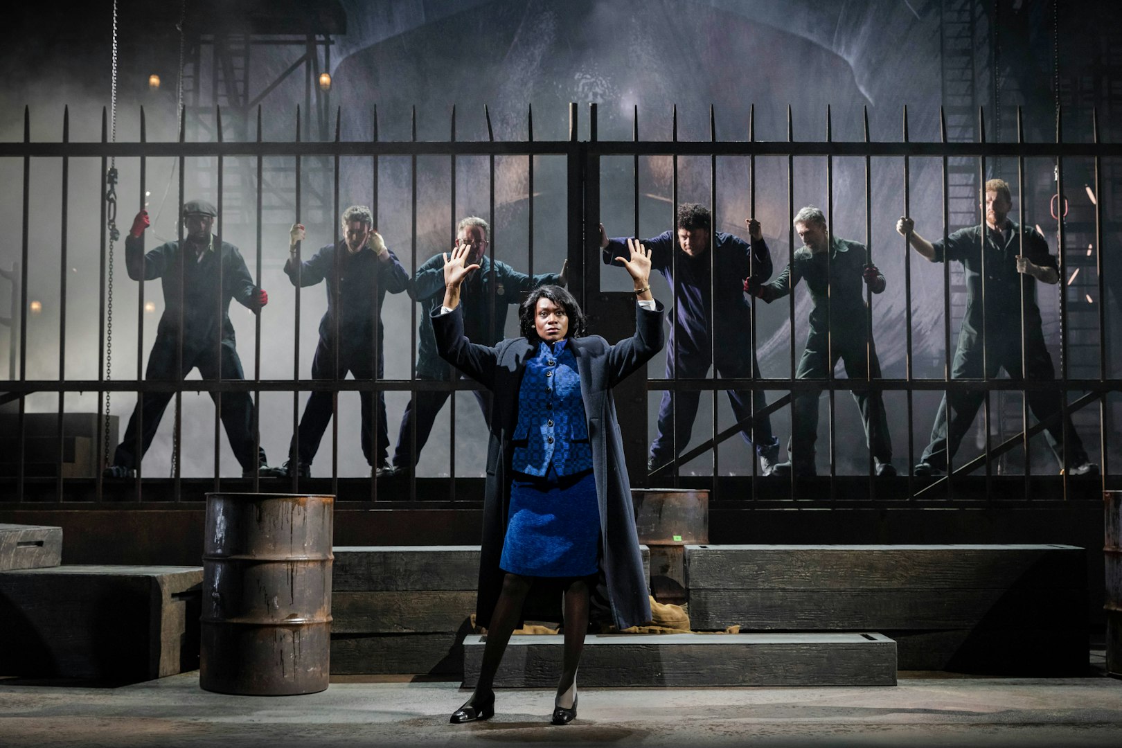 Stage scene from "The Last Ship" in Brisbane with actors behind a metal fence.