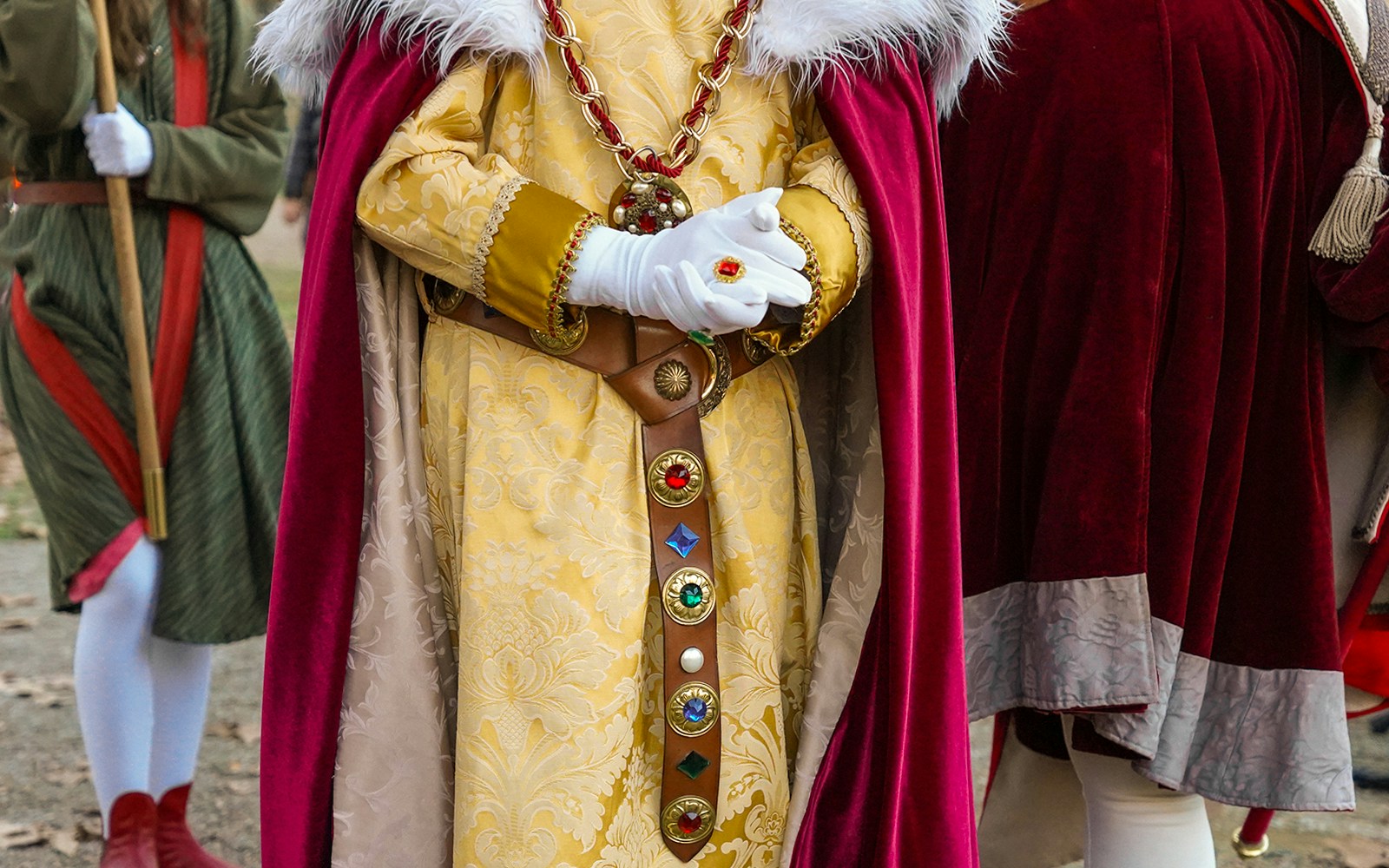 Medieval reenactor in ornate costume with red cape and jeweled belt.