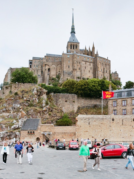 Mont Saint-Michel with tourists in the foreground, featuring the abbey and surrounding buildings.