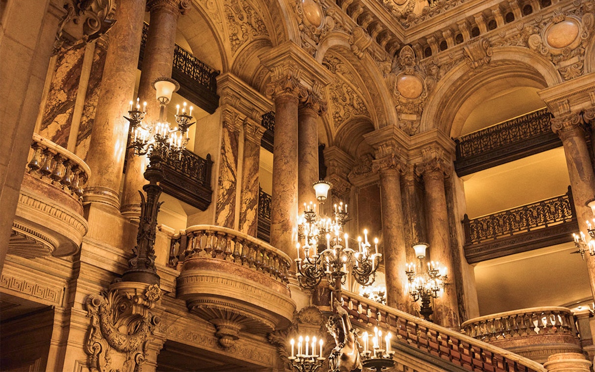 Garnier Opera's grand staircase with ornate chandeliers, Paris, featured in Arsene Lupin Immersive Game.