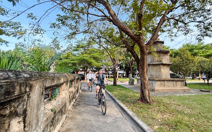Tour group biking past a white chedi and temple on a backstreets tour in Bangkok.