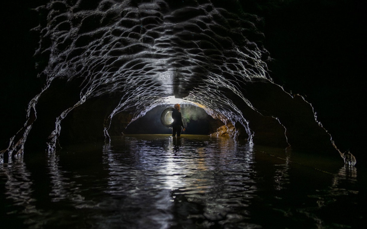 Person exploring Okohua Glowworm Cave with inner tube, Waitomo Experience.