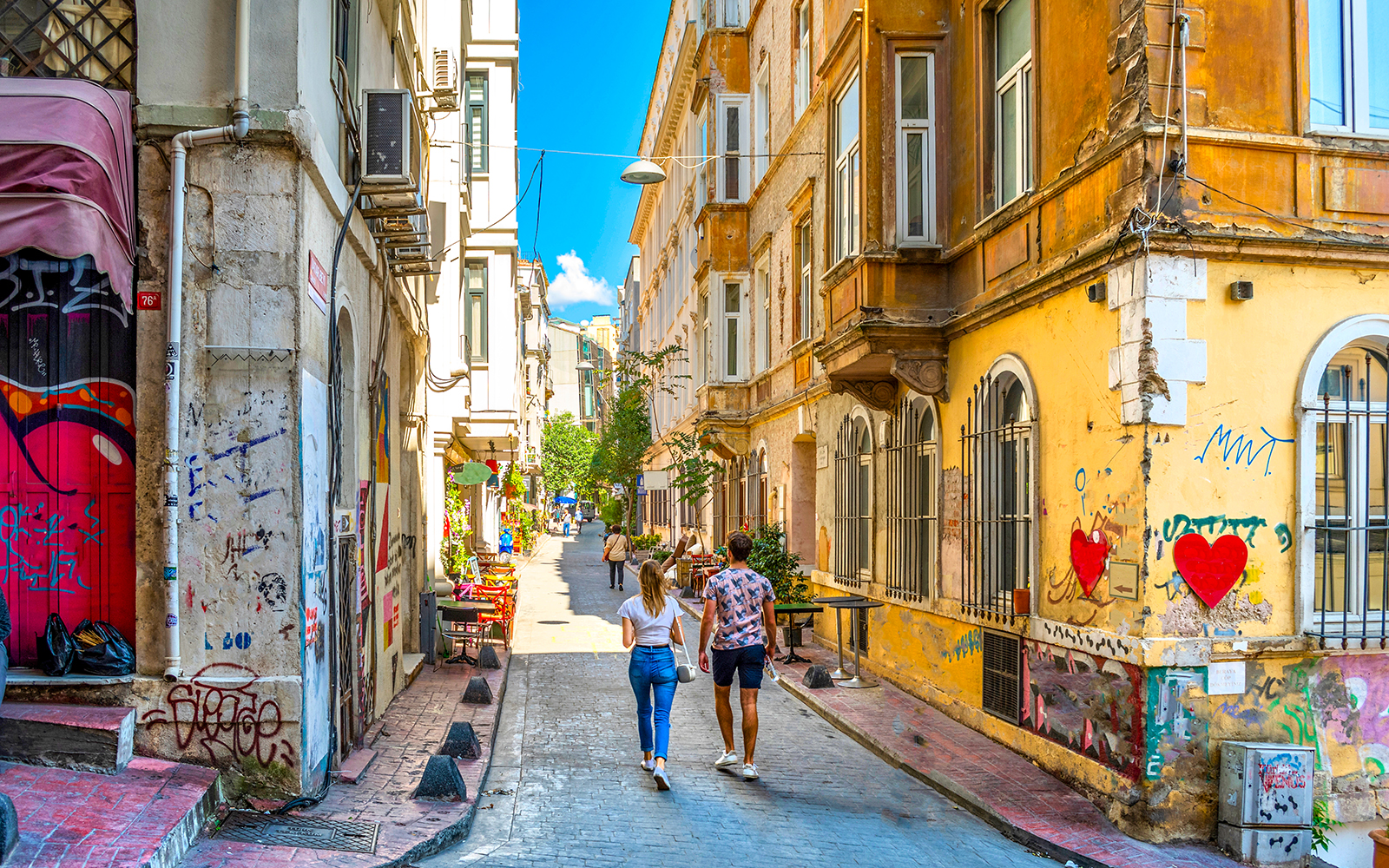 Young couple walking through a colorful alley in Beyoğlu, Istanbul, with street art and historic buildings.