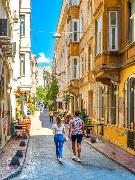 Young couple walking through a colorful alley in Beyoğlu, Istanbul, with street art and historic buildings.