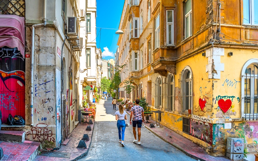 Young couple walking through a colorful alley in Beyoğlu, Istanbul, with street art and historic buildings.