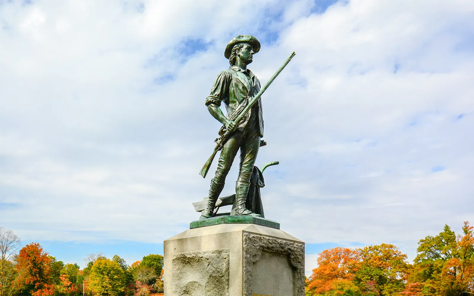 Minuteman Statue in Concord, Boston with autumn trees in the background.