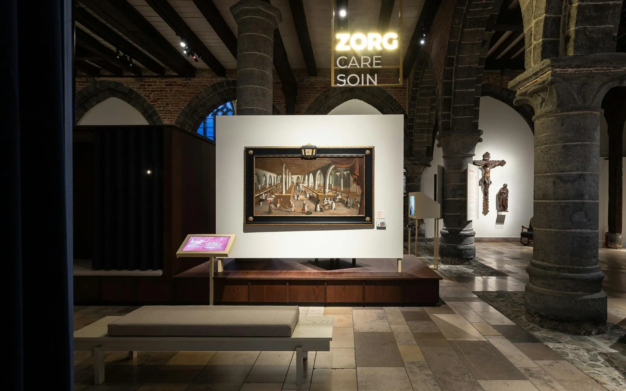Painting display inside Museum Sint-Janshospitaal, Bruges, with historical architecture and art exhibits.