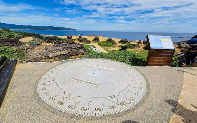Large stone compass overlooking coastal landscape at Yehliu Geopark, New Taipei City, Taiwan.