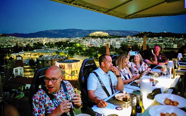 Guests dining at a suspended table with a view of Athens and the Acropolis in the background.