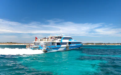 Tourists on a ferry near Rottnest Island with coastline view, part of the guided bus tour.
