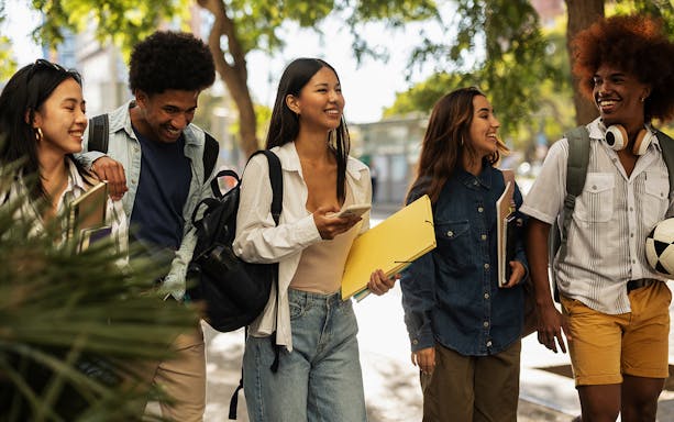 Group of friends walking on a sunny street in Barcelona, carrying books and a soccer ball.