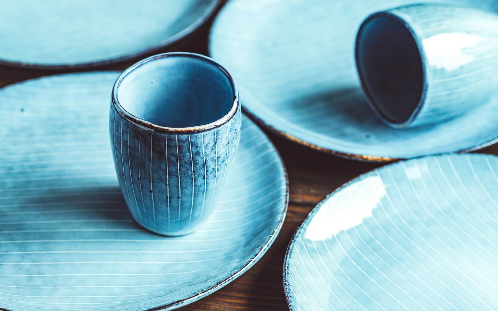 Ceramic plates and cups with blue glaze on a wooden table.