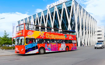 Colorful hop on hop off bus in front of modern building in Tallinn.