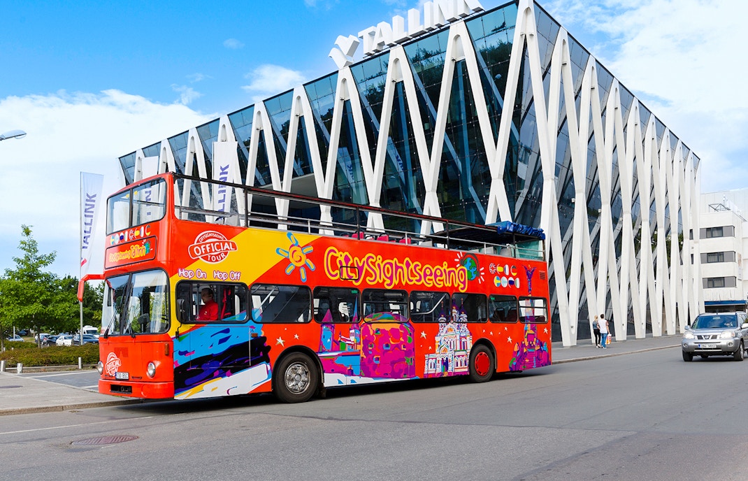 Colorful hop on hop off bus in front of modern building in Tallinn.
