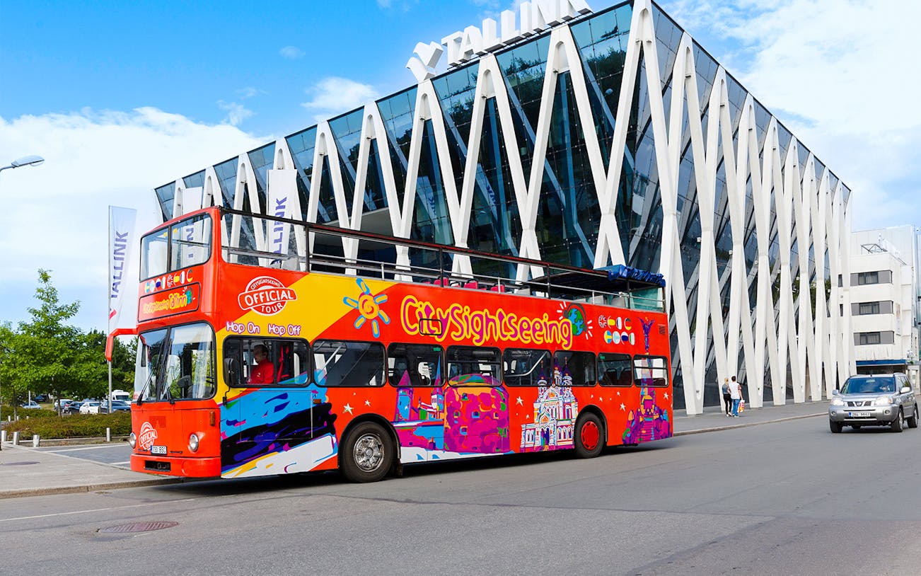 Colorful hop on hop off bus in front of modern building in Tallinn.