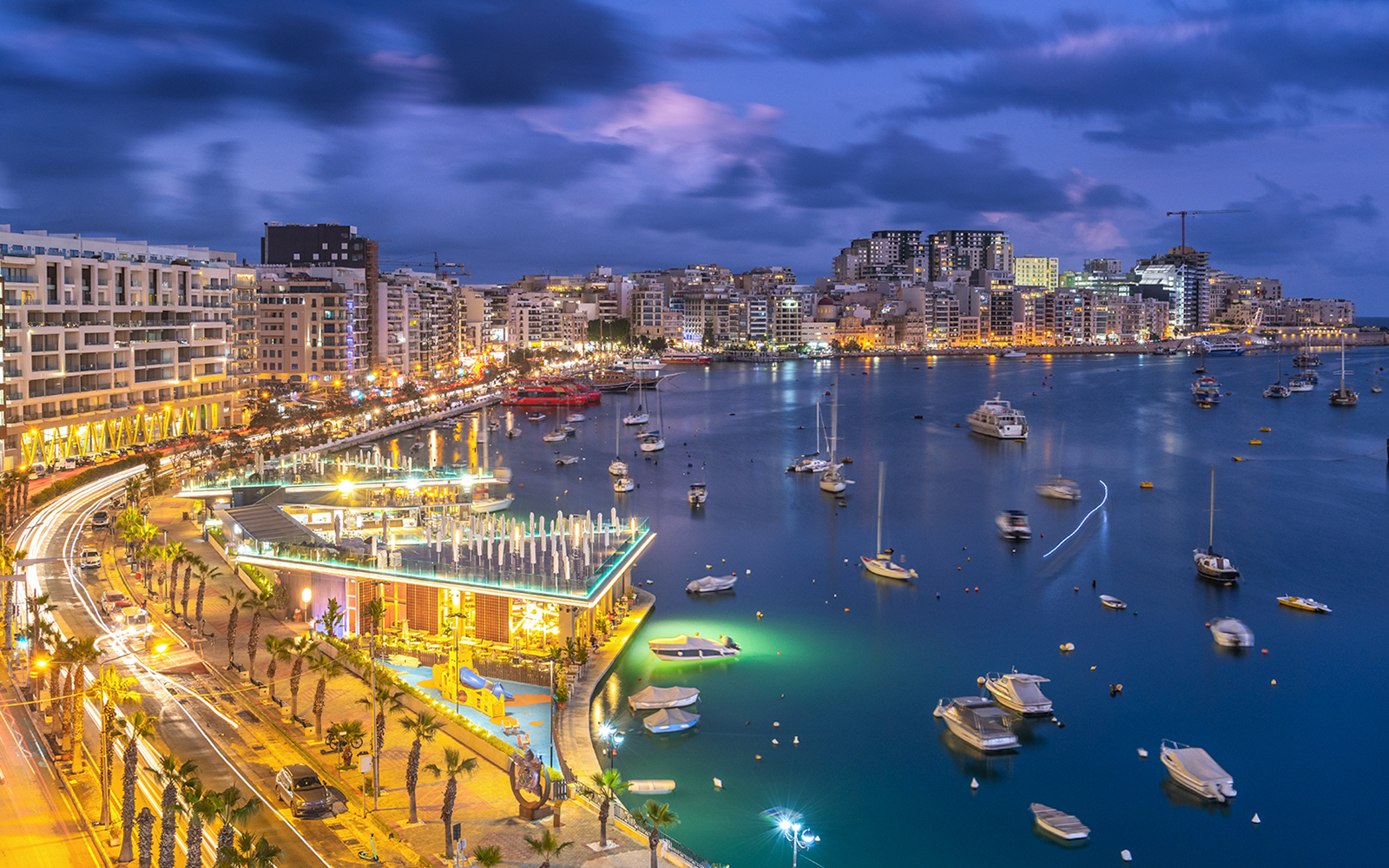 Night view of Sliema Bay, Malta with illuminated waterfront and boats.