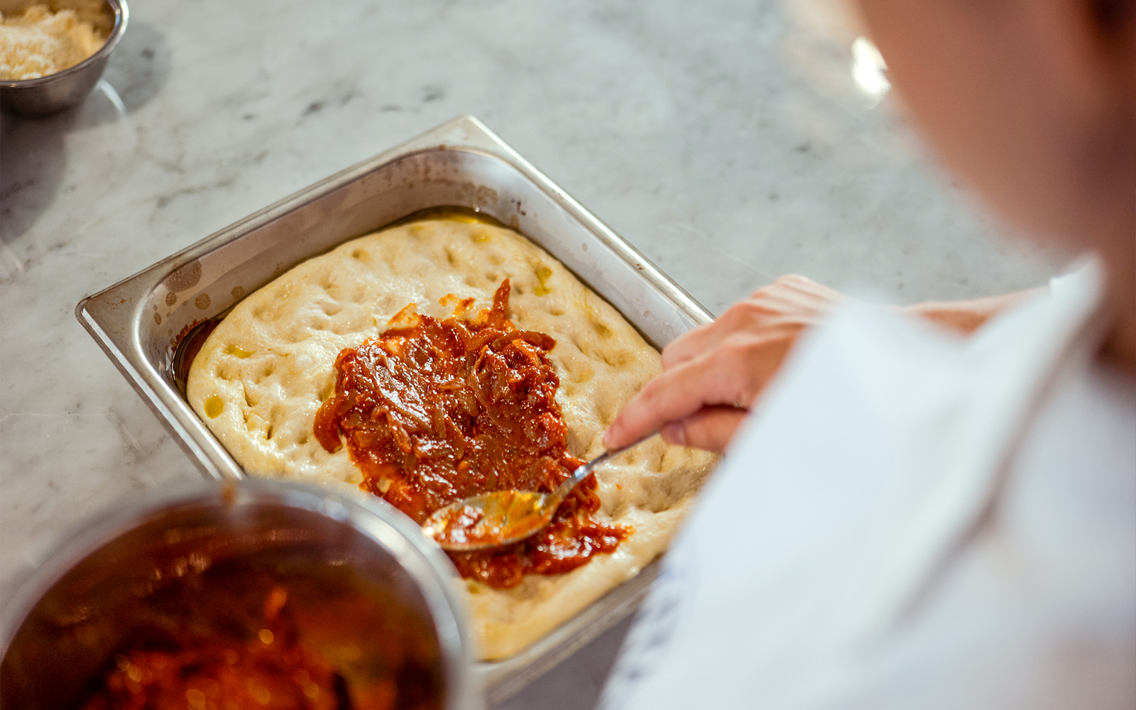 Spreading tomato sauce on pizza dough during cooking class in Palermo.