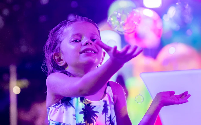Child enjoying colorful lights and bubbles at AquaGlow, Water Country USA.