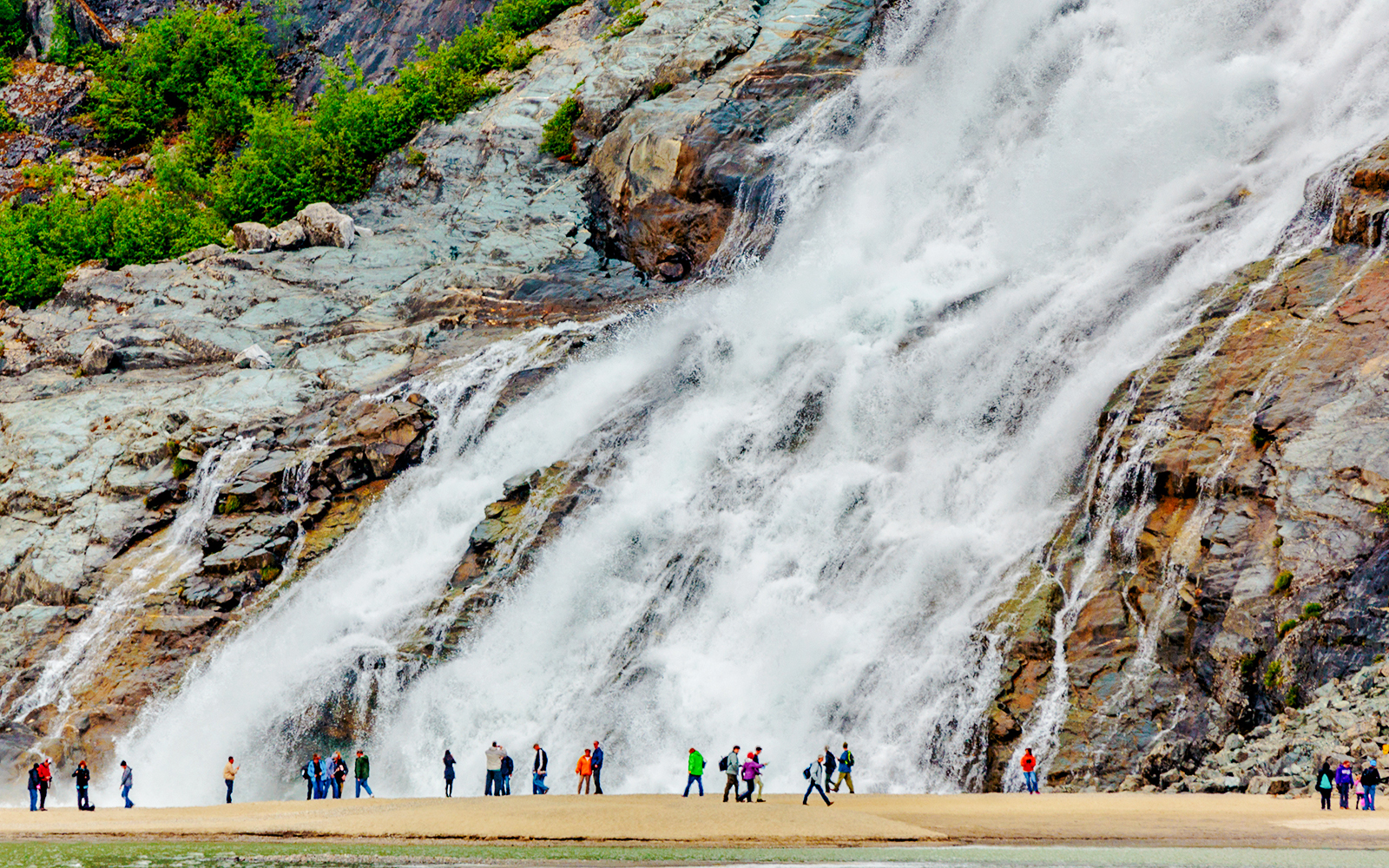 Visitors standing near Nugget Falls waterfall in Juneau, Alaska.