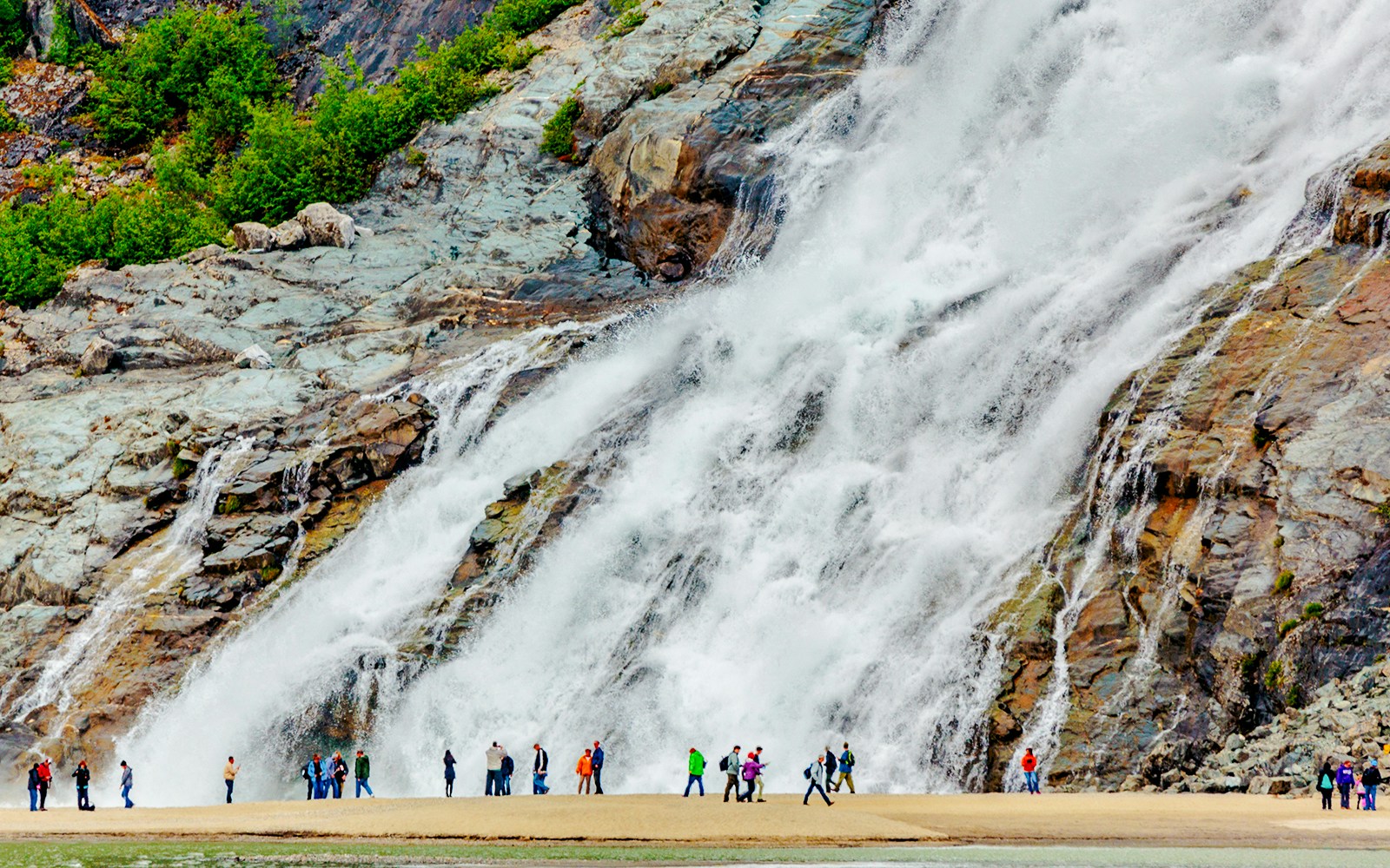 Visitors standing near Nugget Falls waterfall in Juneau, Alaska.
