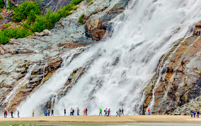 Visitors standing near Nugget Falls waterfall in Juneau, Alaska.