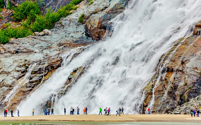 Visitors standing near Nugget Falls waterfall in Juneau, Alaska.