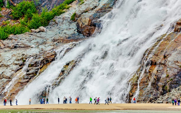 Visitors standing near Nugget Falls waterfall in Juneau, Alaska.
