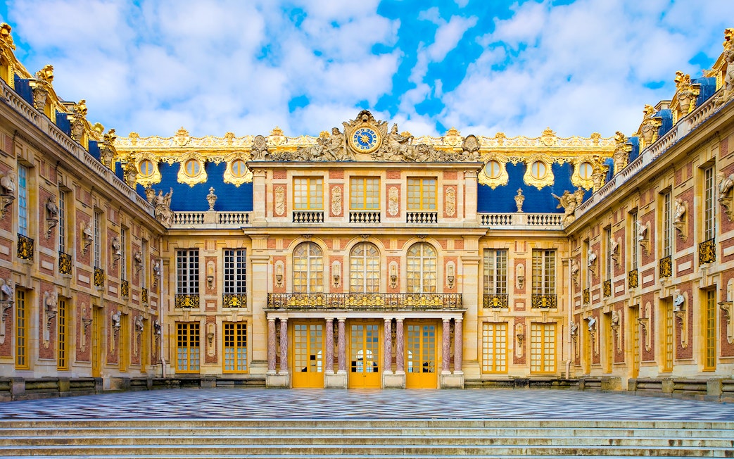Versailles Palace courtyard with ornate architecture and blue sky.