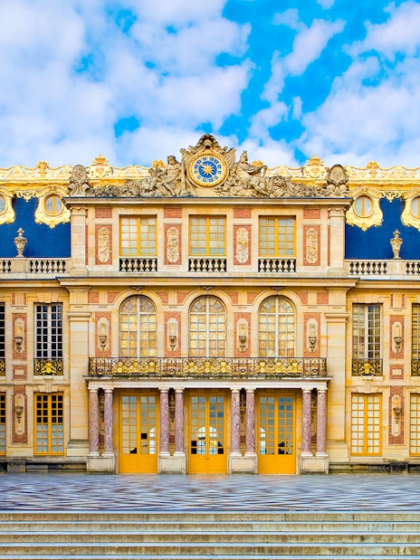 Versailles Palace courtyard with ornate architecture and blue sky.