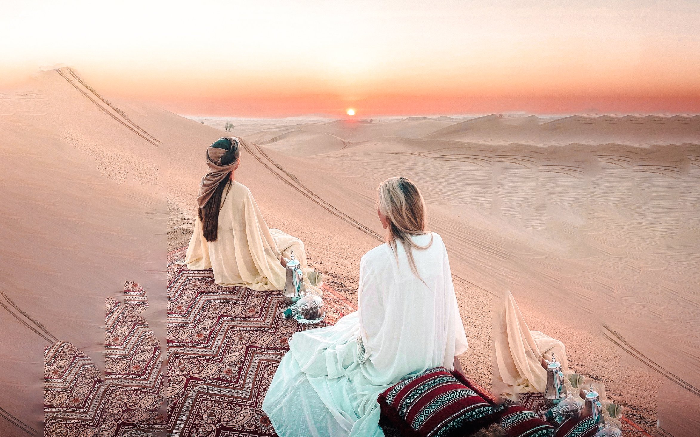 Two people sitting on a carpet in Abu Dhabi desert at sunrise during a morning safari.